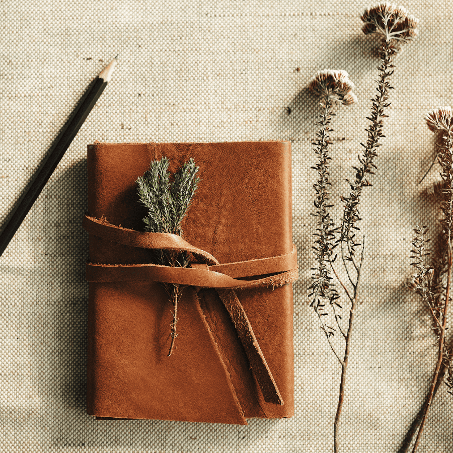 suede bound journal and pencil with dried flowers scattered around.